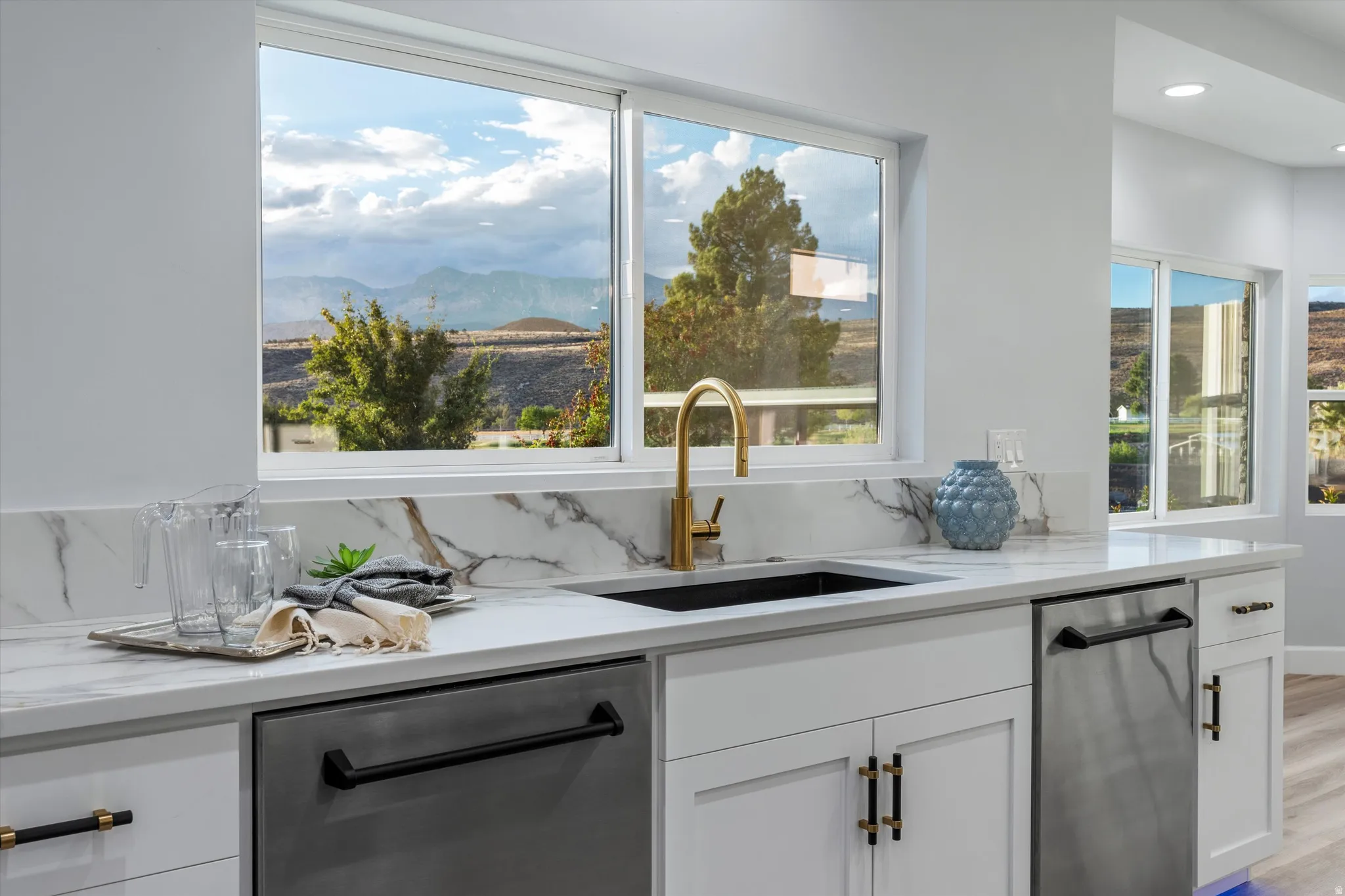 White cabinetry with black and gold hardware, marble-finish countertops, undermount sink with gold-finish faucet, and integrated stainless steel appliances