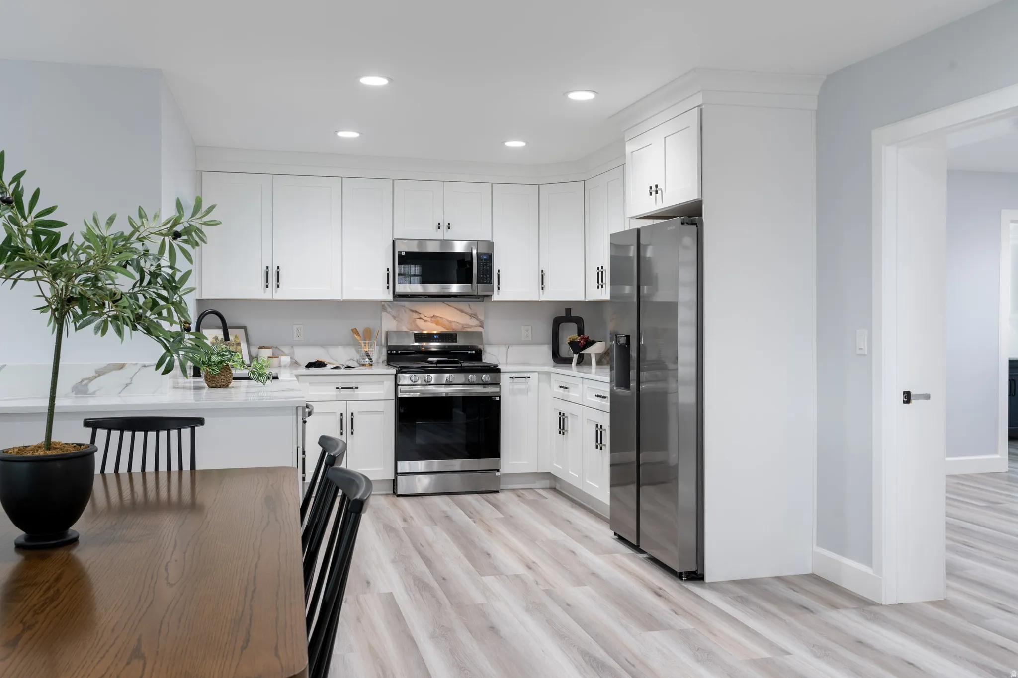 White cabinetry with black hardware, stainless steel appliances, recessed lighting, wood-finish flooring, and light-toned countertops with a matching backsplash