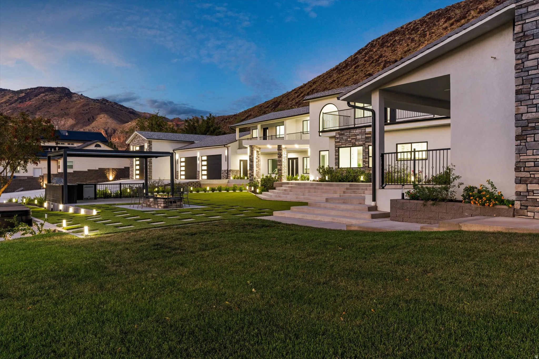 Expansive lawn with integrated stepping stones, a built-in outdoor kitchen with a pergola, and a central fire pit surrounded by seating
