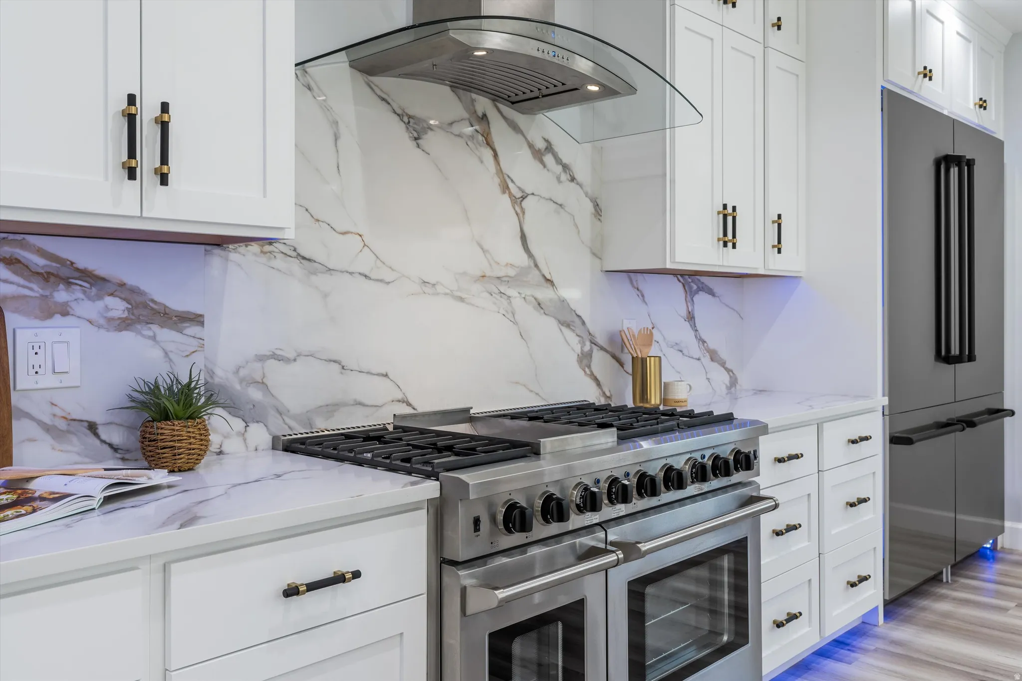 White shaker cabinetry with gold and black hardware, stainless steel professional-grade range, stainless steel refrigerator, white countertops with veining, and a matching backsplash