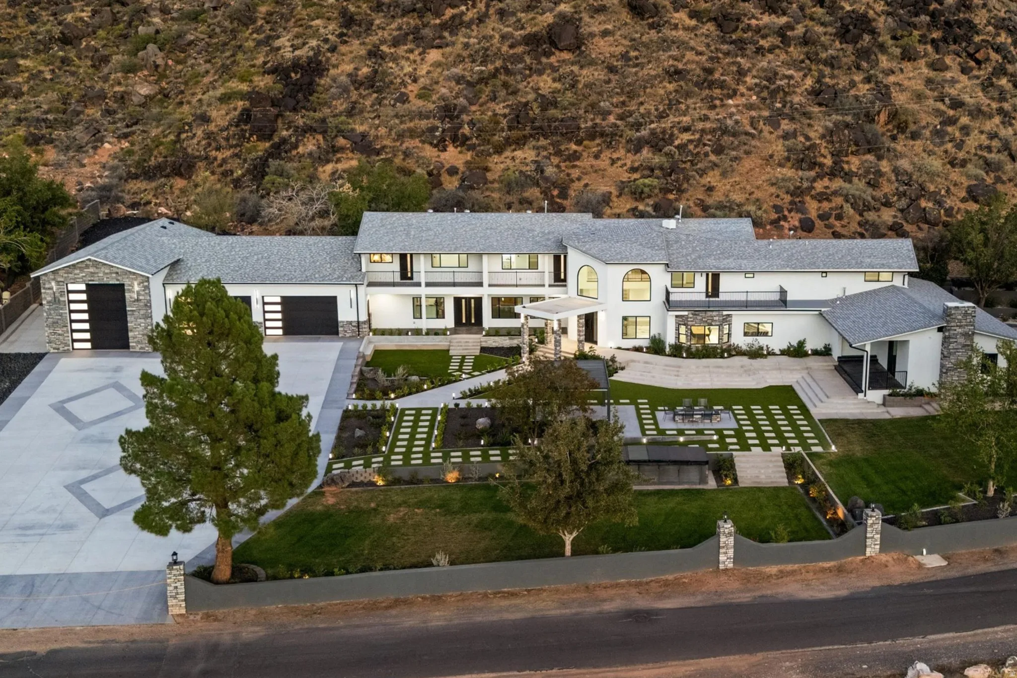 Expansive estate featuring a stucco exterior, three-car garage, multiple balconies, and a meticulously landscaped yard with a geometric patio design