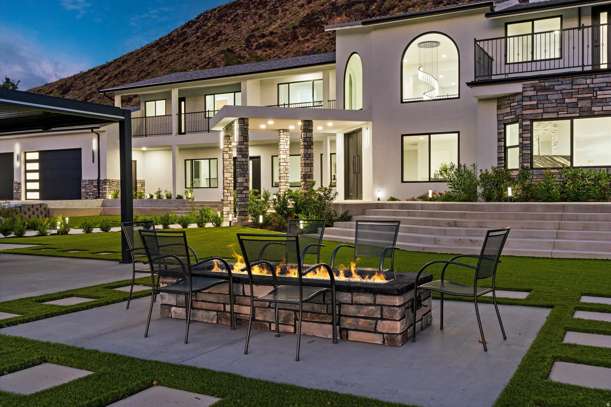 Tiered concrete steps, stone veneer accents, modern exterior lighting, a built-in stone fire pit, and a spacious concrete patio with integrated lawn pavers