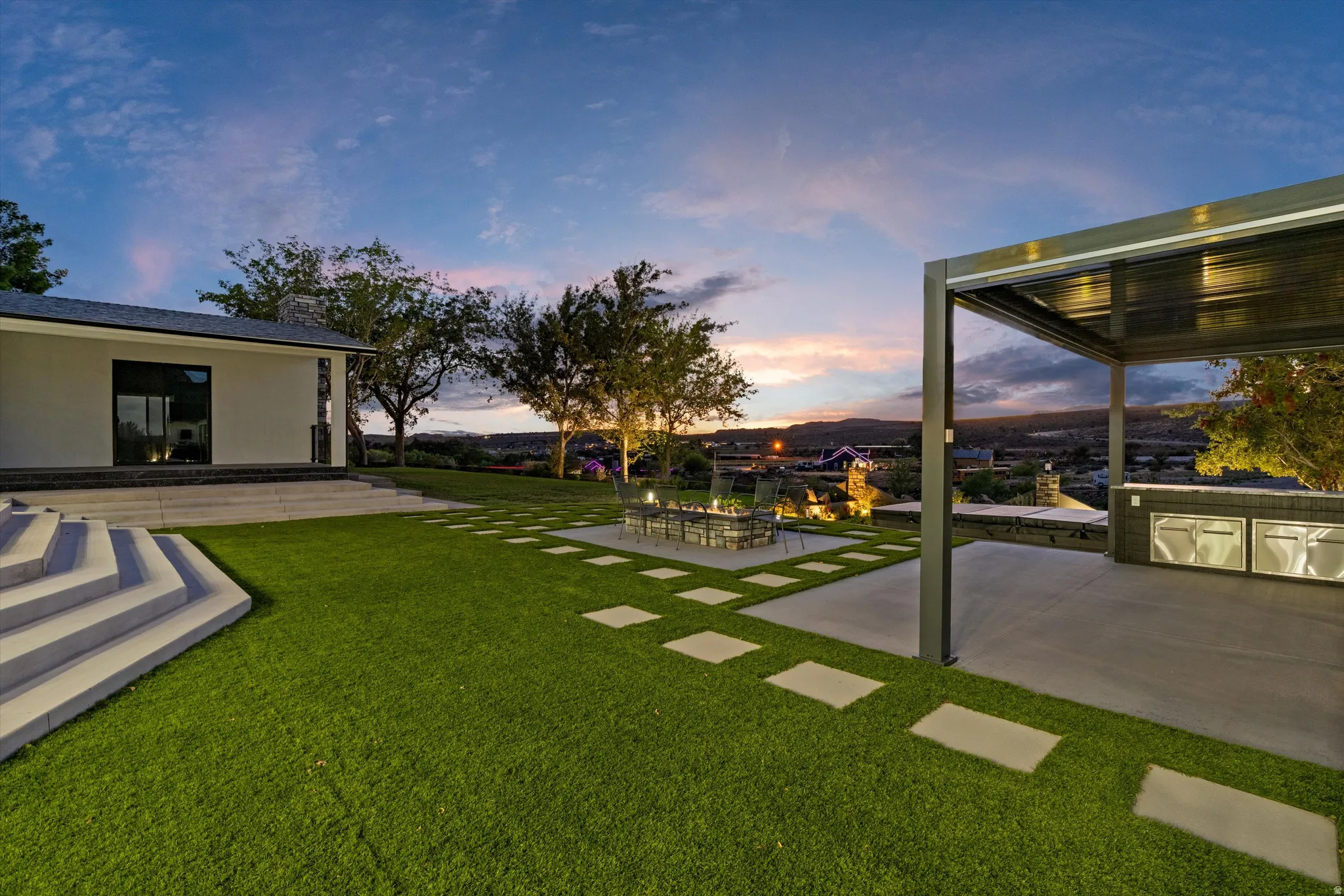 Expansive lawn with integrated stepping stones, a dedicated fire pit area, and a covered outdoor kitchen featuring built-in appliances