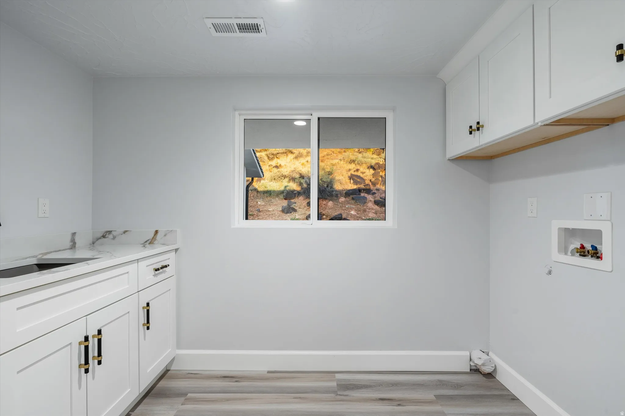 Integrated laundry area featuring white cabinetry with gold-tone hardware, wood-finish flooring, a utility sink with a faucet, and a countertop