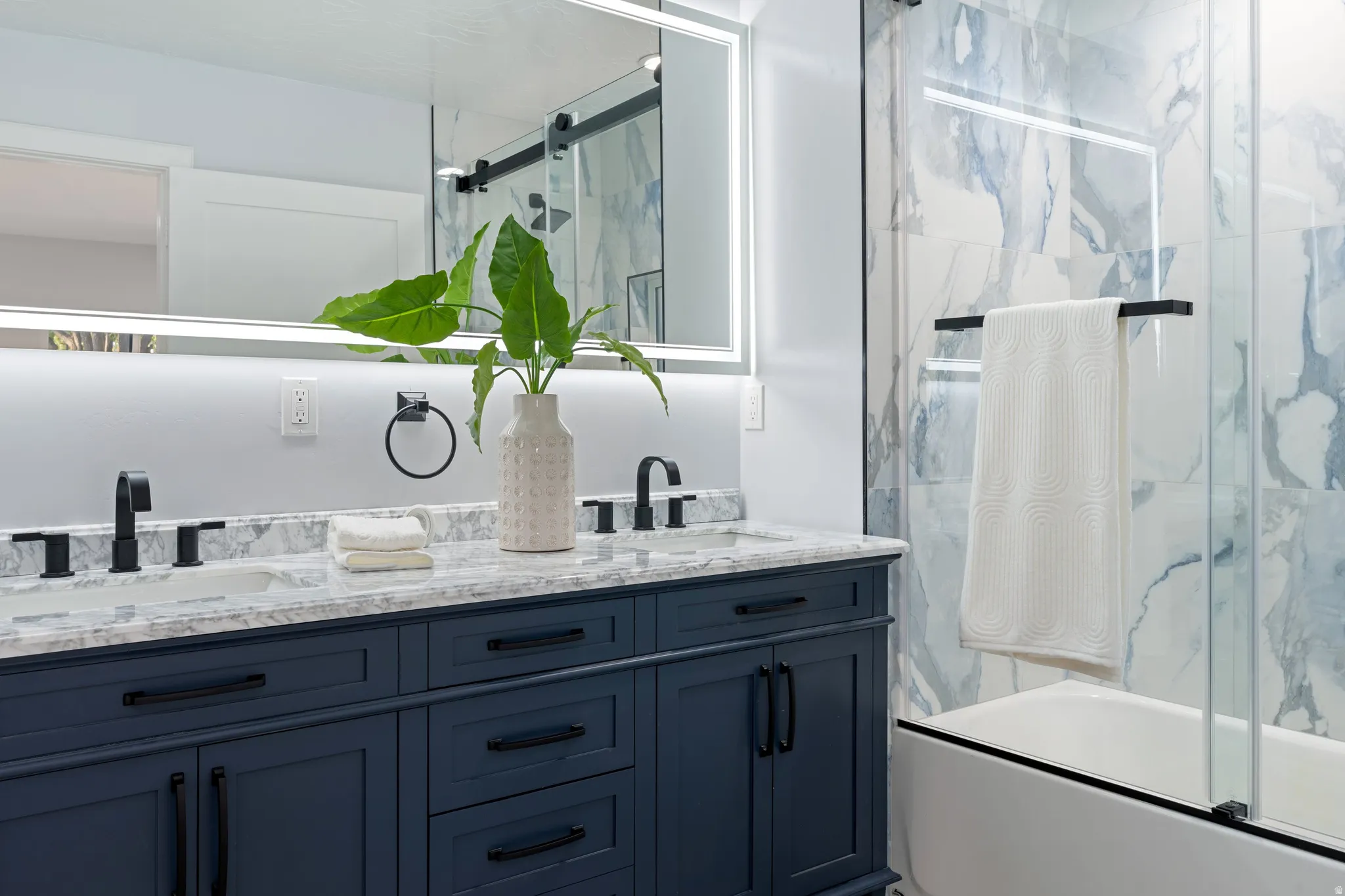 Dual vanity with granite countertop, matte black fixtures, integrated lighted mirror, and deep blue cabinetry