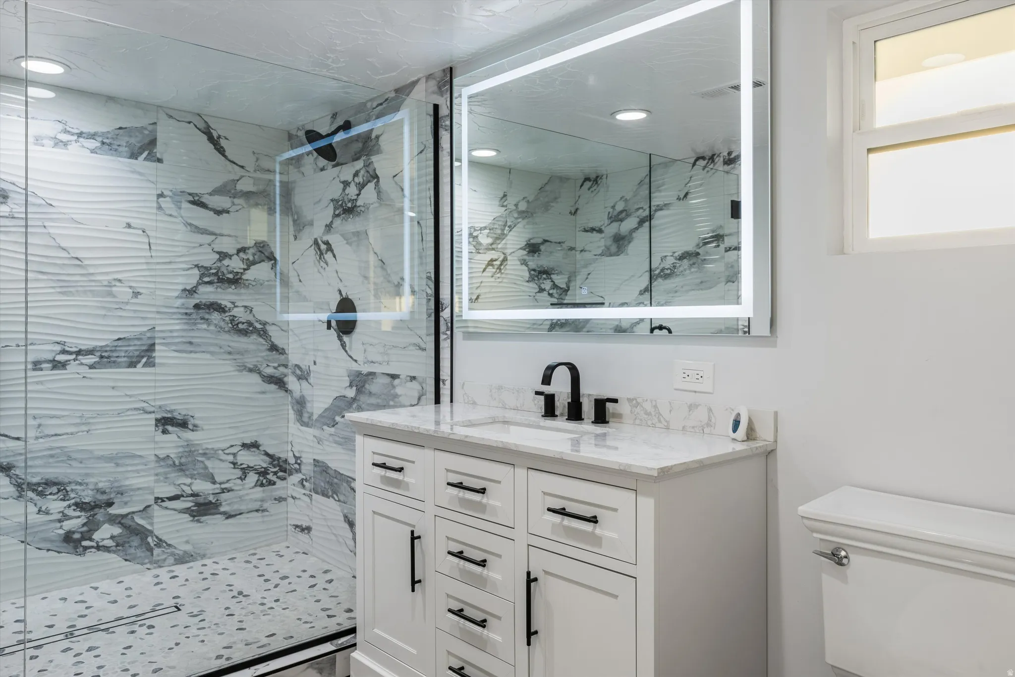 Walk-in shower with textured and marbled-patterned tile, glass enclosure, and black-finish fixtures