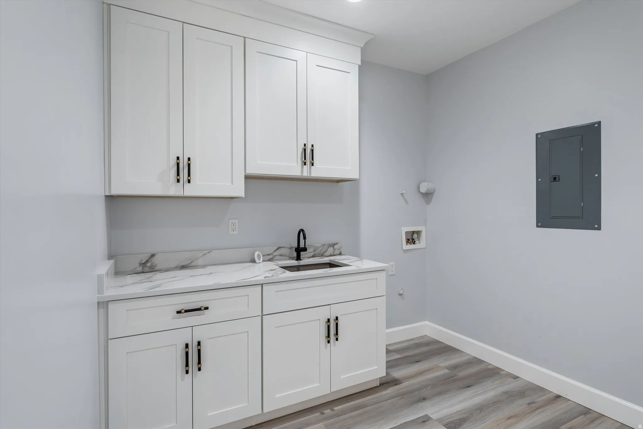 White shaker-style cabinetry with matte black hardware, quartz-finish countertop, undermount sink with a matte black faucet, and wood-finish flooring