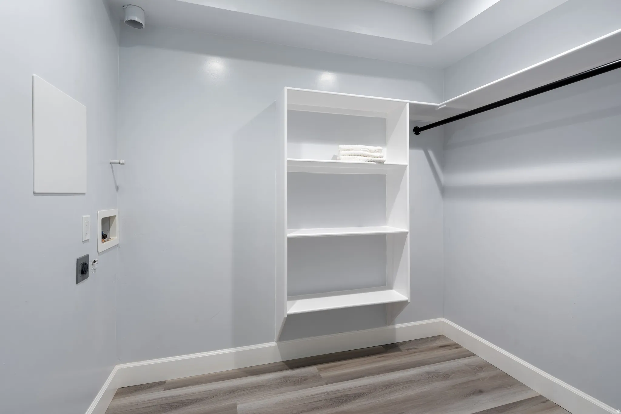 White built-in shelving, black hanging rod, wood-finish flooring, white baseboards, and light-toned wall paint