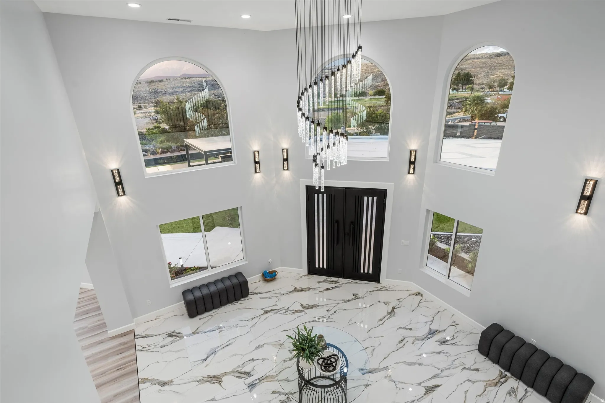 Double-height entryway featuring a contemporary chandelier, arched windows, and a double entry door