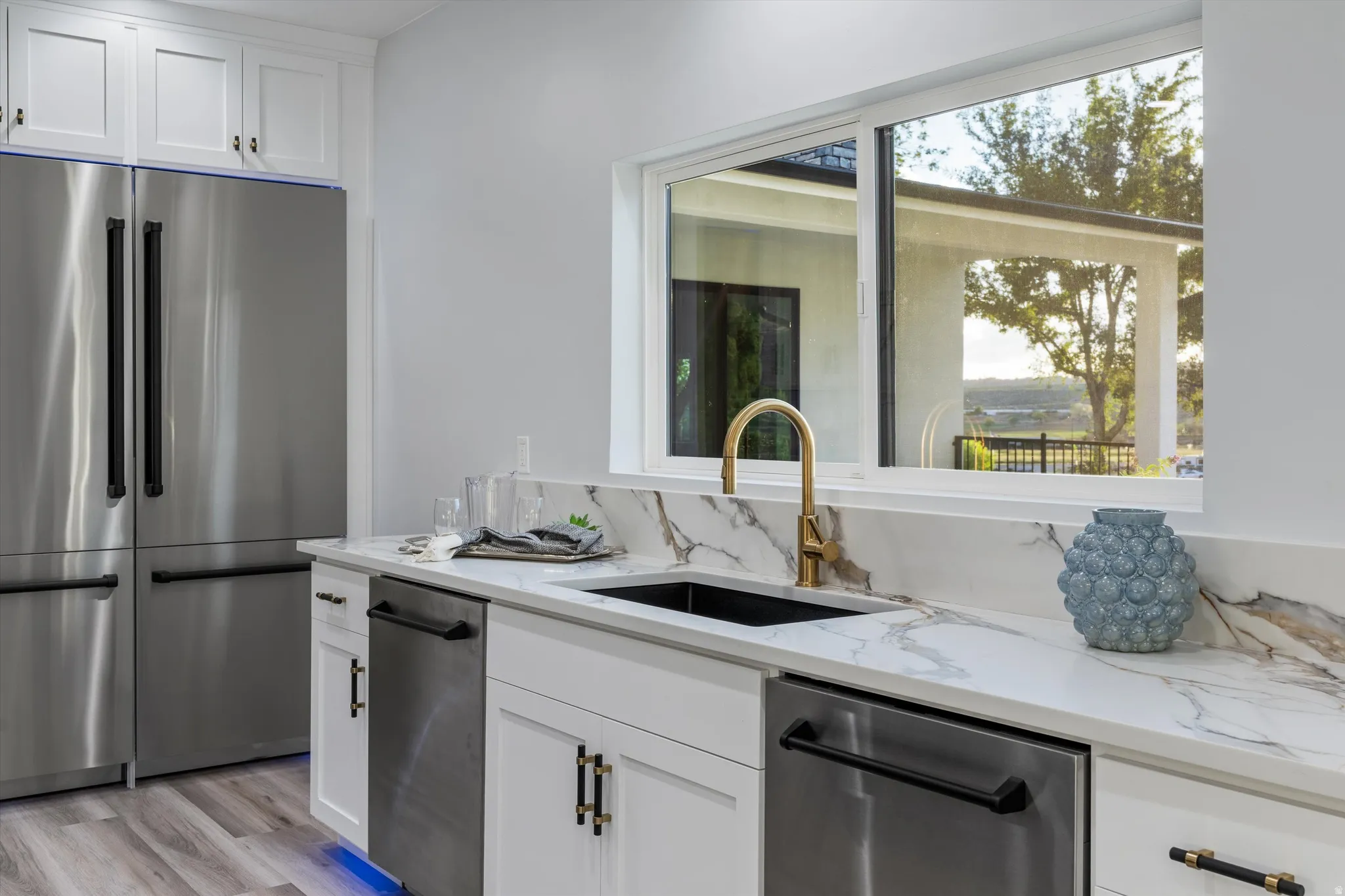 Stainless steel appliances, white cabinetry with dark hardware, stone countertops with a matching backsplash, and wood-finish flooring