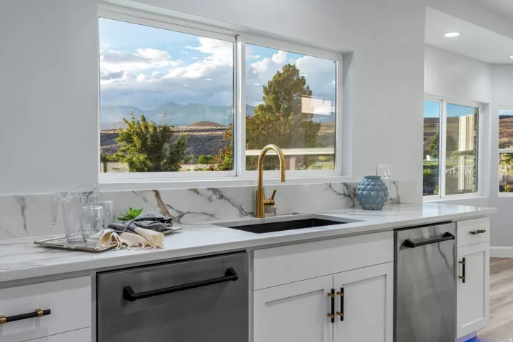 White cabinetry with black and gold hardware, marble-finish countertops, undermount sink with gold-finish faucet, and integrated stainless steel appliances
