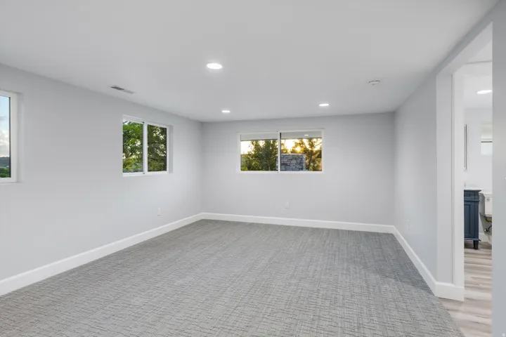 Recessed lighting, light-colored walls, multiple windows, patterned carpeting, and an adjoining space with wood-finish flooring