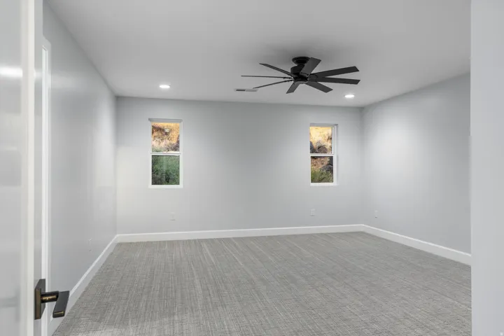 Recessed lighting, ceiling fan with matte black blades, two rectangular windows, gray patterned carpeting, and white trim
