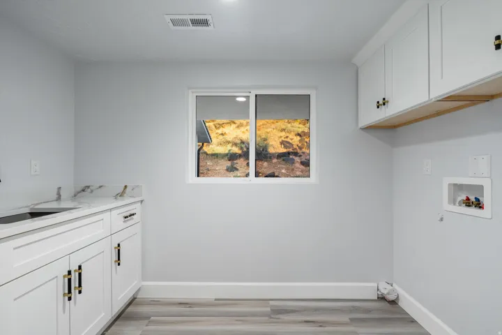 Integrated laundry area featuring white cabinetry with gold-tone hardware, wood-finish flooring, a utility sink with a faucet, and a countertop