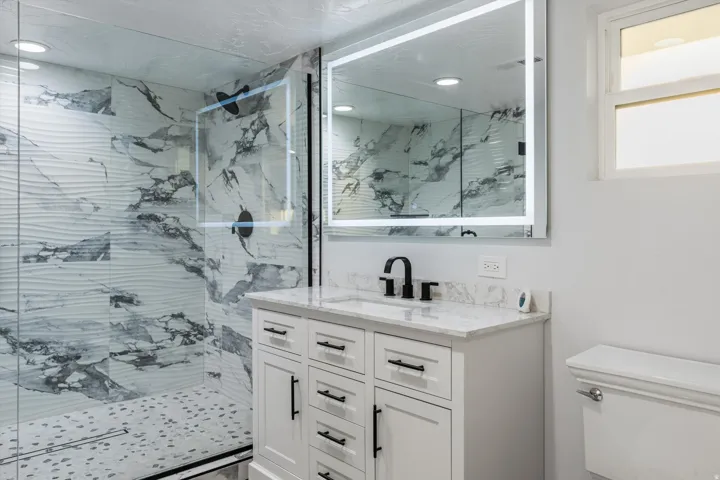 Walk-in shower with textured and marbled-patterned tile, glass enclosure, and black-finish fixtures