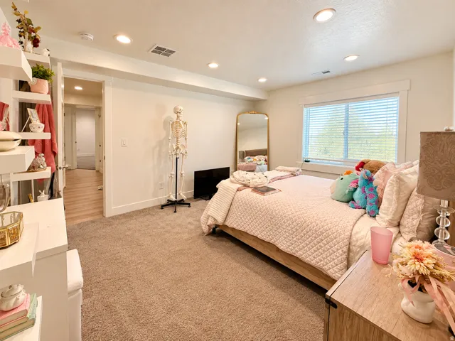 Recessed lighting illuminates the room, featuring a carpeted floor and a window with blinds