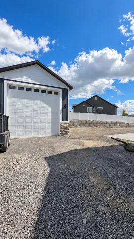 Detached garage with white paneled door, stone facade base, and gravel driveway