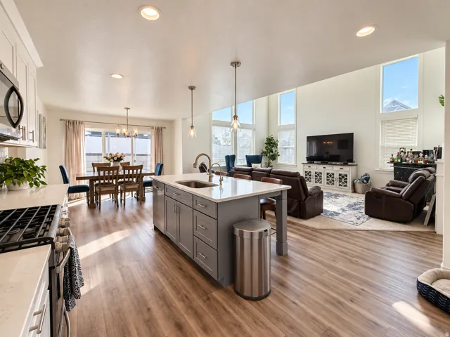 Open-concept living area featuring wood-finish flooring, a kitchen island with seating, recessed lighting, and high ceilings with tall windows