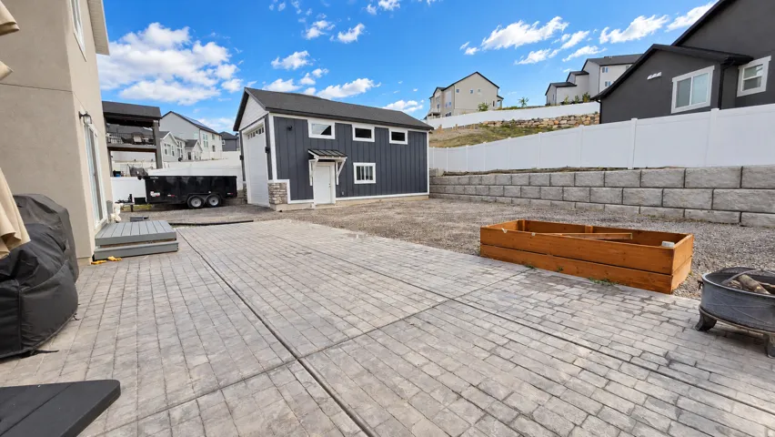 Stamped concrete patio with a detached auxiliary building featuring board and batten siding, stone veneer accents, and a roll-up garage door