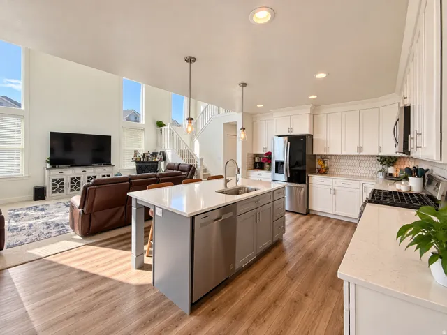Open-concept living space featuring wood-finish flooring, a two-story ceiling, a kitchen island with seating, stainless steel appliances, and white cabinetry