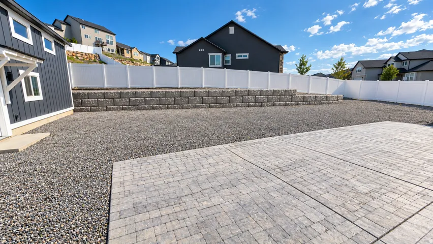 Paver patio area, gravel landscaping, white privacy fencing, and a stone retaining wall