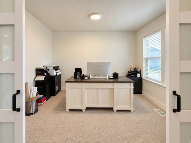 Room featuring neutral-toned carpeting, white walls, a large window with blinds, and white sliding doors with frosted glass panels and black hardware