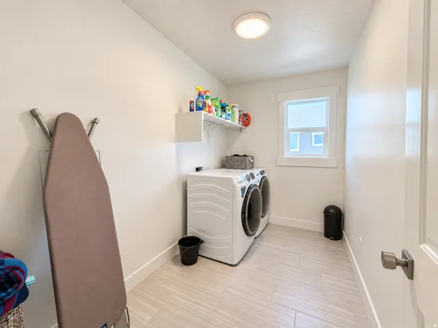Utility room with light-toned rectangular floor tiles, a window with trim, a ceiling-mounted light fixture, and white painted walls