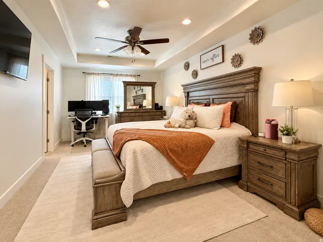 Tray ceiling with recessed lighting and a ceiling fan, light-colored walls, window with blinds and sheer curtains, light-toned carpet flooring, and a built-in desk area