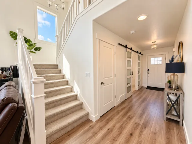 Wood-finish flooring, white paneled doors, dual barn doors with frosted glass panels, an entry door with glass inserts, and a carpeted staircase
