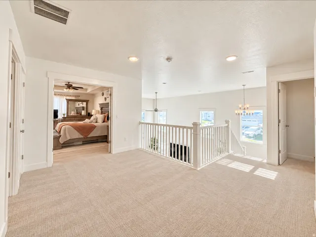 Open landing area with neutral carpeting, white baluster railing, recessed lighting, and a chandelier fixture