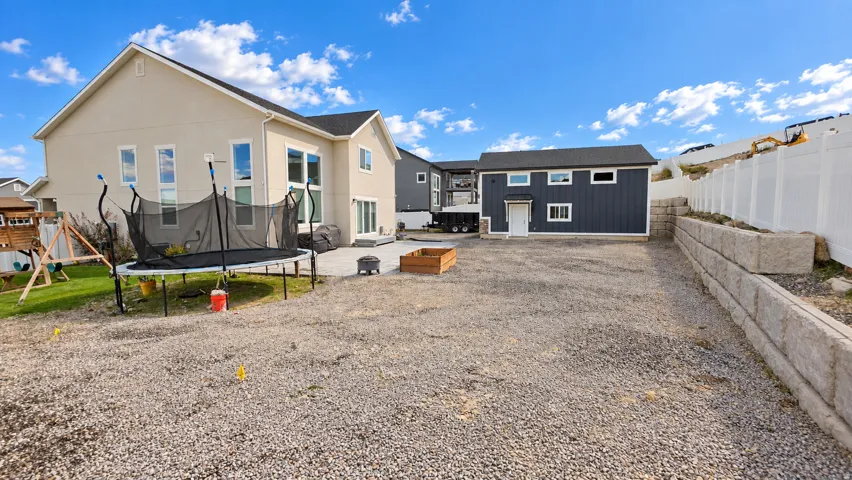 Stucco exterior with multiple windows, concrete patio, gravel area, retaining wall, and a detached structure with siding