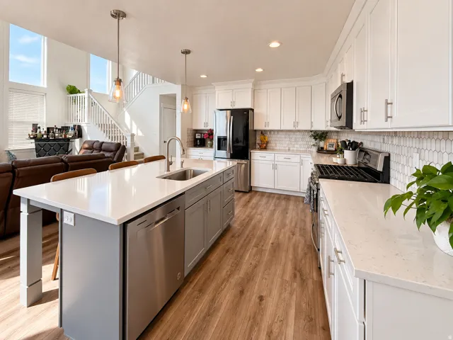 Kitchen featuring an expansive island with a stainless steel sink, wood-finish flooring, white cabinetry, integrated appliances, and a tiled backsplash