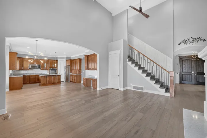 Vaulted ceilings, wood-finish flooring, staircase with wrought iron railing, arched doorway, and a kitchen with wood cabinetry