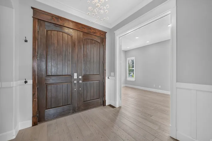 Double wood entry doors with dark wood trim, white wainscoting, and light wood-finish flooring