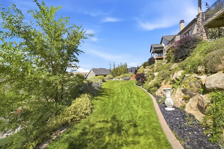Terraced landscaping with a manicured lawn, established plantings, and rock retaining walls