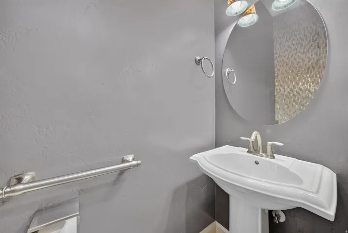 Pedestal sink with brushed nickel faucet, round mirror, and wall-mounted light fixture