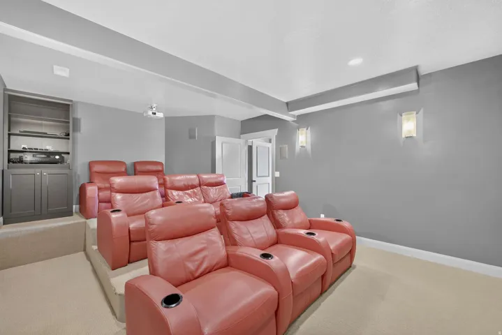 Tiered home theater with built-in media cabinetry, wall sconces, ceiling-mounted projector, and neutral carpeting