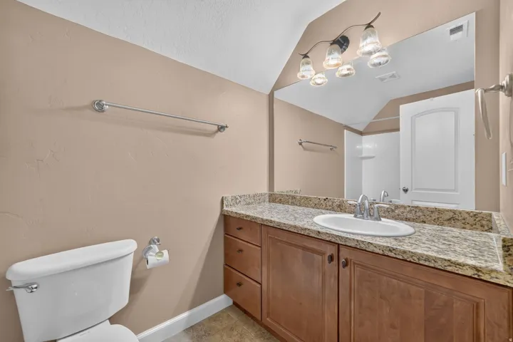 Vanity with a granite-style countertop, undermount sink, and wood-finish cabinetry