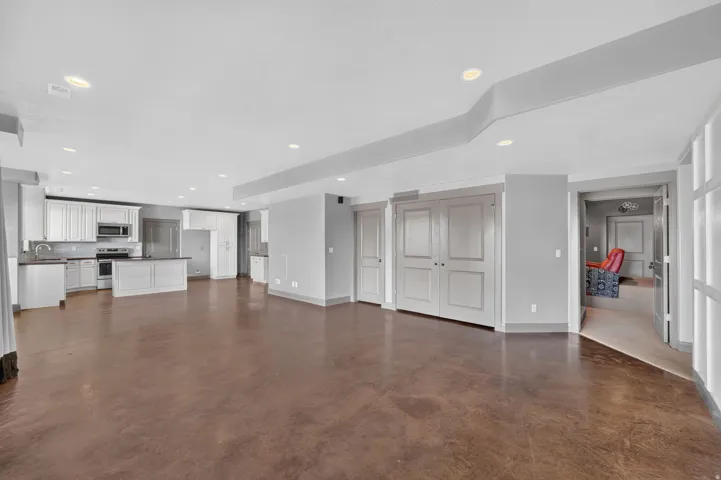 Open-concept living space featuring rich brown flooring, recessed lighting, and a kitchen with white cabinetry and stainless steel appliances