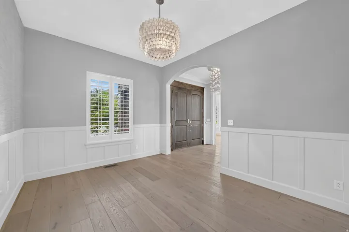Wood-finish flooring, wainscoting, decorative pendant light fixture, window with plantation shutters, and an arched entryway