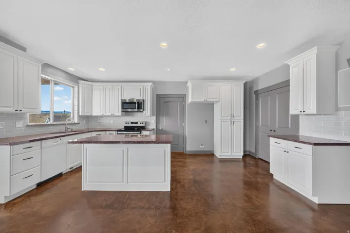 Spacious kitchen featuring white cabinetry, a center island, an undermount sink, and stainless steel appliances