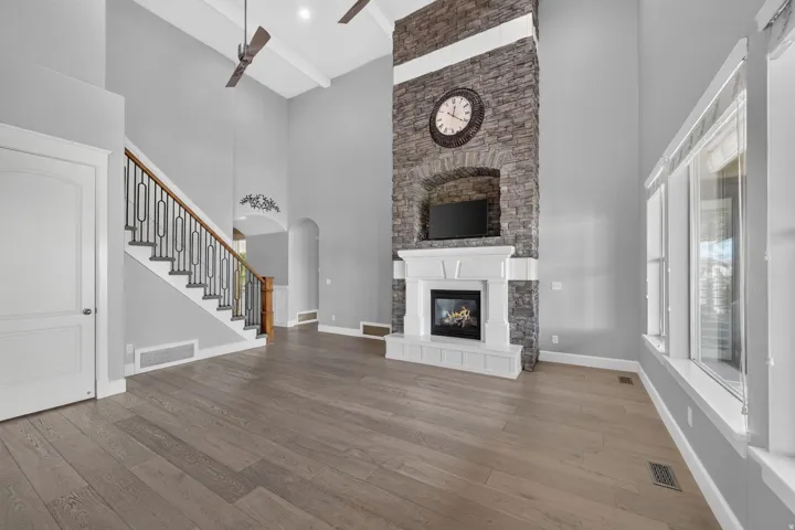 Soaring vaulted ceilings, wood-finish flooring, and a stone-clad fireplace with a white mantel