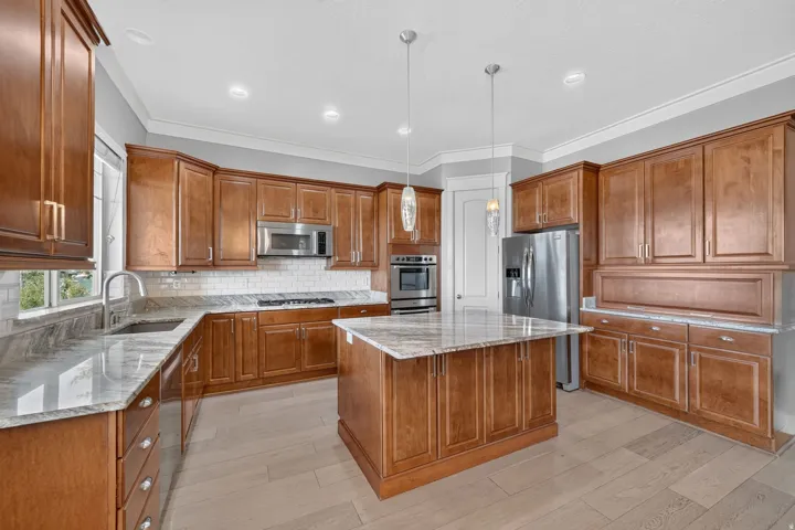 Kitchen featuring wood-finish cabinetry, light-toned wood-finish flooring, island with countertop, stainless steel appliances, and subway tile backsplash