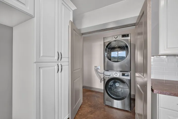 White shaker-style cabinetry, stainless steel stacked washer and dryer, subway tile backsplash, and composite countertop