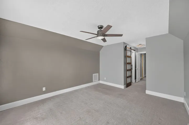 Sloped ceiling room featuring a ceiling fan, plush carpet flooring, and a modern barn door with glass panels