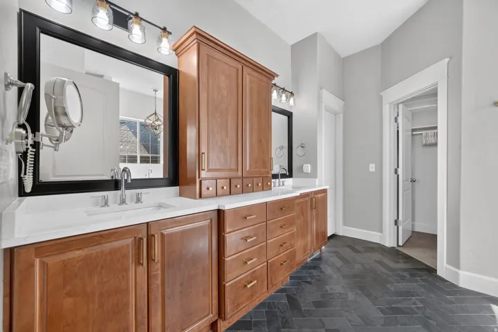 Double vanity with wood-finish cabinetry, white countertops, black-framed mirrors, and herringbone tile flooring