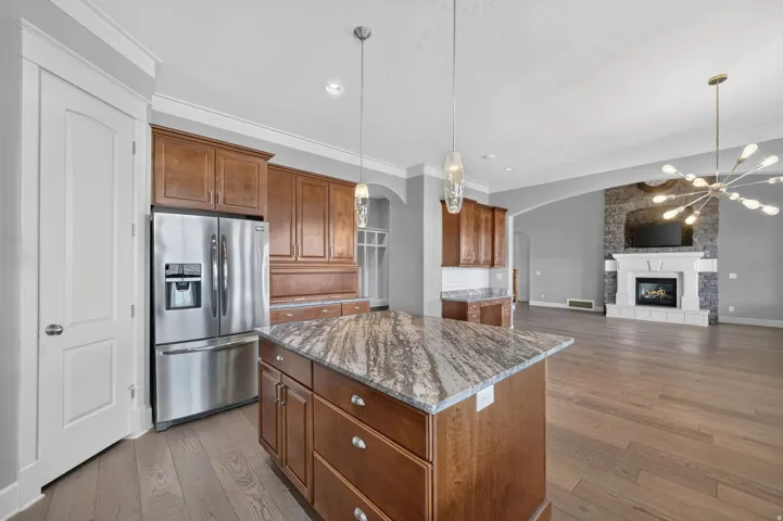Stainless steel refrigerator, custom wood cabinetry, a central island with a stone countertop, wood-finish flooring, and a fireplace with a stone surround