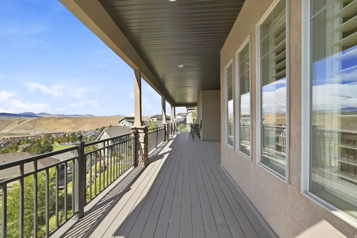 Expansive covered balcony featuring composite decking, metal railings, stone-wrapped columns, and exterior stucco finish