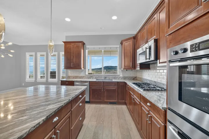 Kitchen featuring wood-finish flooring, custom cabinetry, stainless steel appliances, a tiled backsplash, and stone countertops