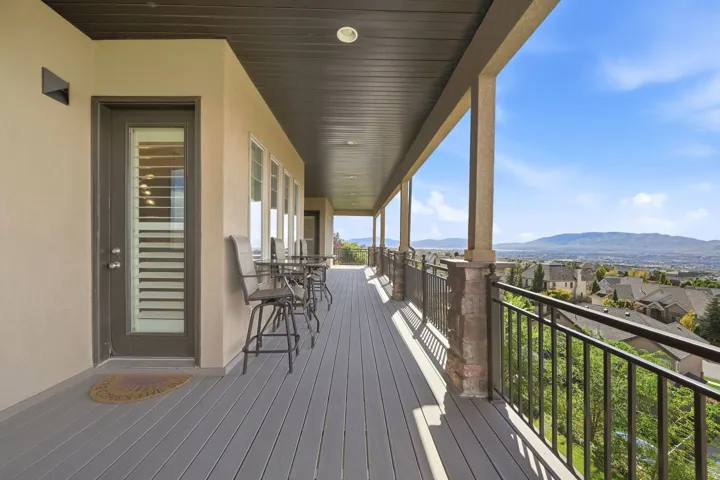 Expansive covered balcony featuring a composite deck, wrought iron railings, and stone-clad columns